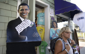 A passer-by, right, departs a store that features cut-outs of President Barack Obama, left, and First Lady Michelle Obama, center, Saturday, Aug. 9, 2014, in Oak Bluffs, Mass., on the island of Martha's Vineyard. President Obama and his family are returning to the island off the Massachusetts mainland Saturday. The president is doing something unusual with his summer vacation on Martha's Vineyard: He'll come back to Washington midway through the getaway to attend White House meetings. (AP Photo/Steven Senne)